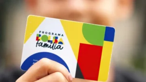 Mãe sorri com bebê no colo segurando cartão do Bolsa Família.