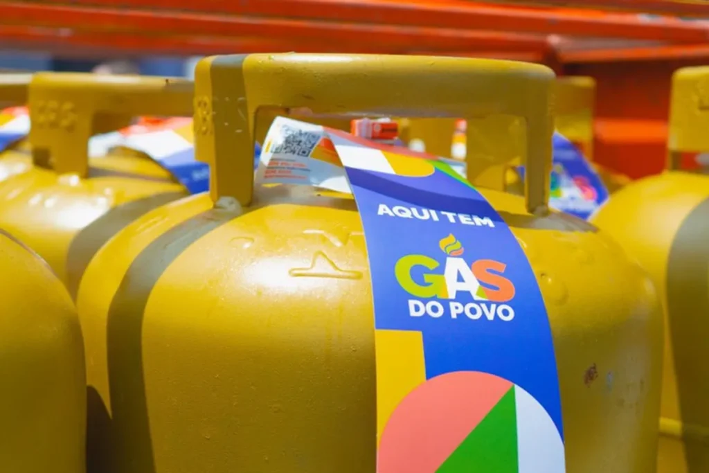 Mulher sorri ao receber botijão de gás recarregado pelo programa Gás do Povo.