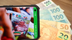 Mulher brasileira consulta aplicativo do Bolsa Família no celular ao lado dos filhos