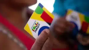 Mulher preocupada olhando extrato do Bolsa Família e celular com notificação