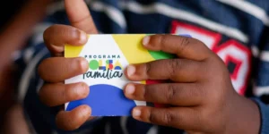 Mulher sorri ao verificar o aplicativo Caixa Tem em seu celular, que exibe informações sobre o Bolsa Família.