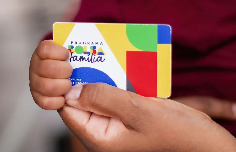 Trabalhadora recebendo cartão do Bolsa Família em agência da Caixa.