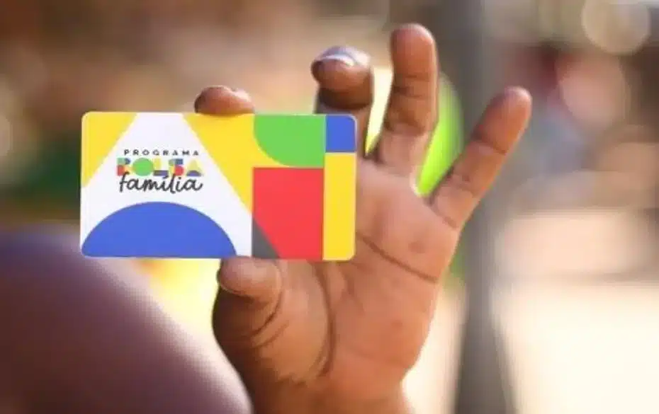 Mão segurando cartão do Bolsa Família com família ao fundo