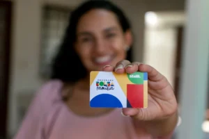 Mulher verifica celular com cartão do Bolsa Família, simbolizando gestão financeira familiar.