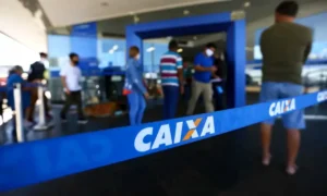 Pessoas em fila em frente a uma casa lotérica, algumas olhando o celular com preocupação.