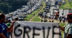 Caminhoneiro olha apreensivo para o preço alto do diesel em um posto de combustível.