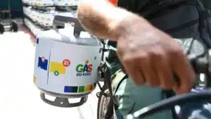 Mulher olha para botijão de gás de cozinha vazio, representando a dificuldade de acesso.