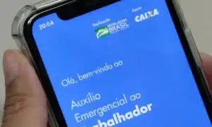 Estudante do ensino médio usando celular em sala de aula, com materiais escolares.