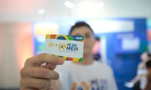 Jovem estudante feliz olhando o celular, possivelmente verificando o pagamento do programa Pé-de-Meia no aplicativo Caixa Tem.