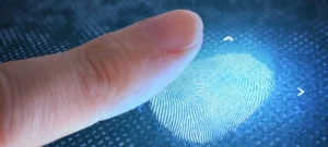 Mão de pessoa registrando biometria em leitor digital, com fundo desfocado de alguém consultando documentos ansiosamente