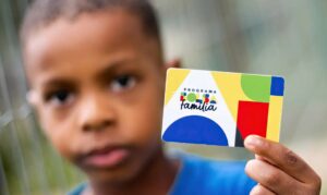Família brasileira em situação de vulnerabilidade recebendo um abono natalino, com decoração de Natal ao fundo.