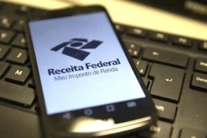 Pessoa idosa revisando documentos financeiros e interagindo com um computador, simbolizando a gestão do Imposto de Renda e os benefícios fiscais.