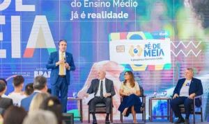 Mão segurando celular com alerta sobre pagamentos de programa social, com estudantes ao fundo.