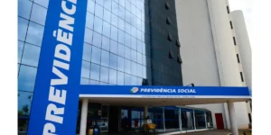 Mão segurando dinheiro com pessoas e tela de computador ao fundo, simbolizando benefícios do INSS e planejamento futuro