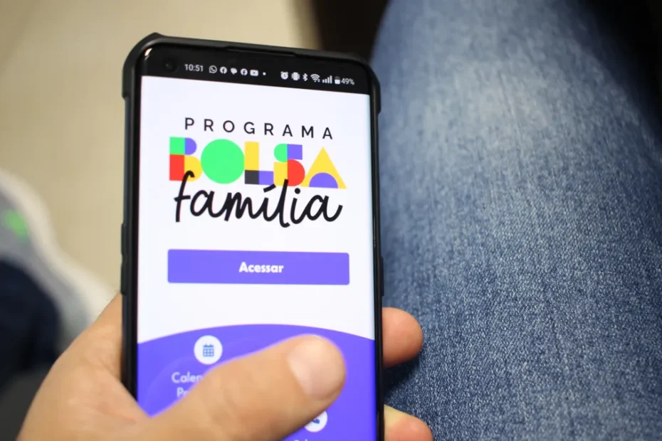 Mão de uma pessoa segurando um smartphone com o aplicativo do Bolsa Família aberto, com foco na tela, enquanto consulta o benefício.