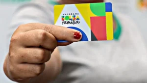 Mão segurando cartão Bolsa Família com calendário ao fundo