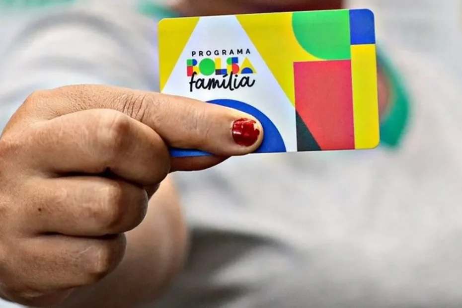 Mão segurando cartão Bolsa Família com calendário ao fundo