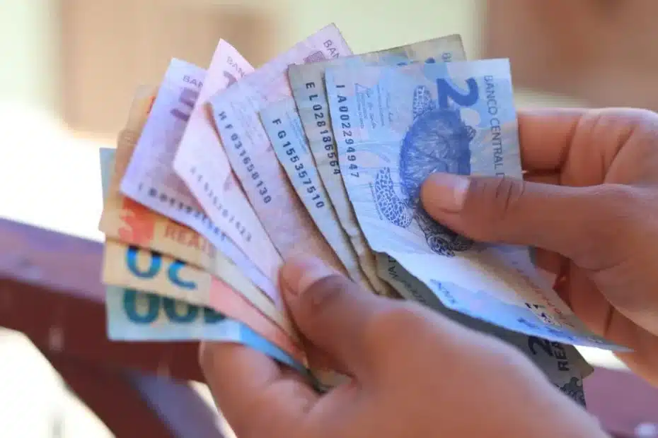 Mãos segurando um celular com aplicativo de apostas e um cartão do Bolsa Família, simbolizando o risco de bloqueio de benefícios.