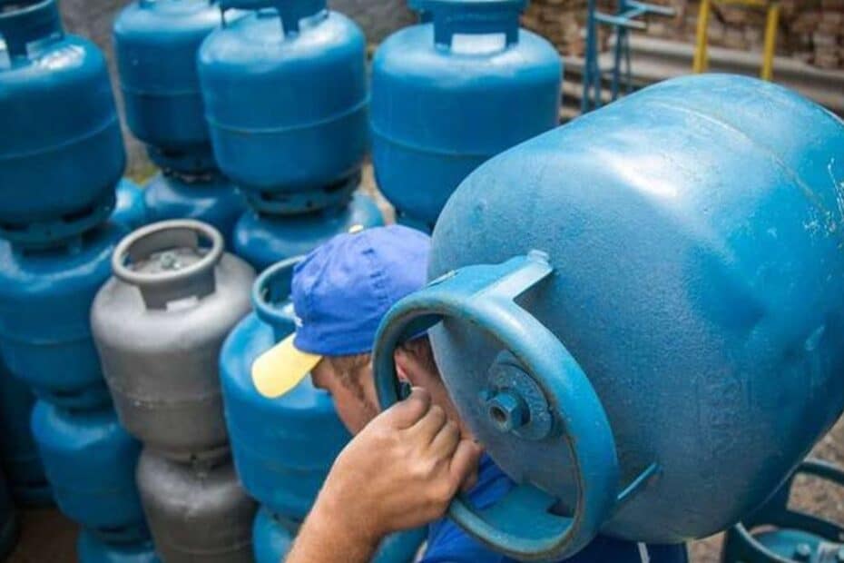 Mão de pessoa segurando um botijão de gás com cédulas de dinheiro, simbolizando o reajuste do Gás do Povo.