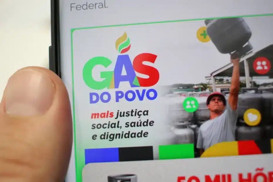 Mão segurando um vale-gás do programa Gás do Povo, com botijões de gás desfocados ao fundo.