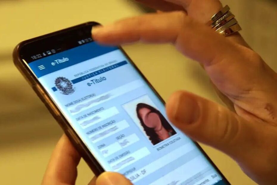 Mãos segurando um título de eleitor e um celular com a tela do TSE sobre regularização