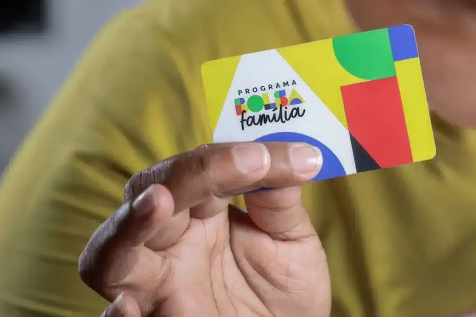 Mulher verifica saldo do Bolsa Família no celular, com um cartão em mãos, simbolizando o dia do pagamento.