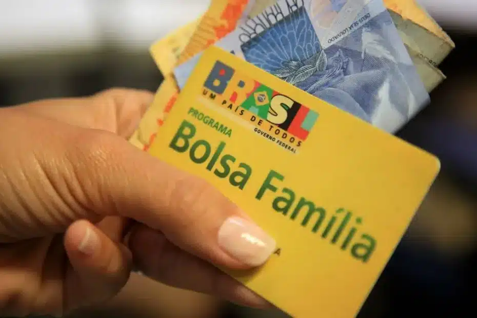 Assistente social realizando entrevista domiciliar com beneficiário do Bolsa Família na entrada de uma casa simples