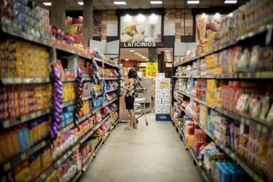 Mão segurando alimentos básicos em frente a prateleira de supermercado