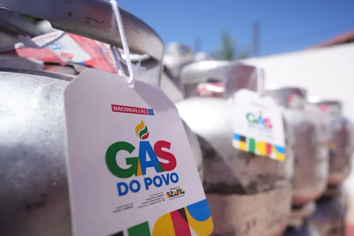 Mãos segurando o botijão de gás azul, representando o Gás do Povo para famílias de baixa renda.