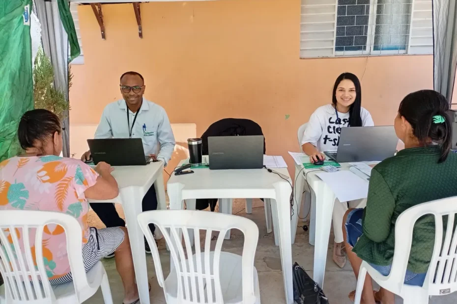Uma mulher segura um documento do Cadastro Único enquanto conversa com um assistente social em um balcão de atendimento.