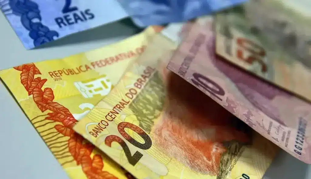 Mãos segurando cartão de benefício do INSS próximo a um celular com o aplicativo oficial