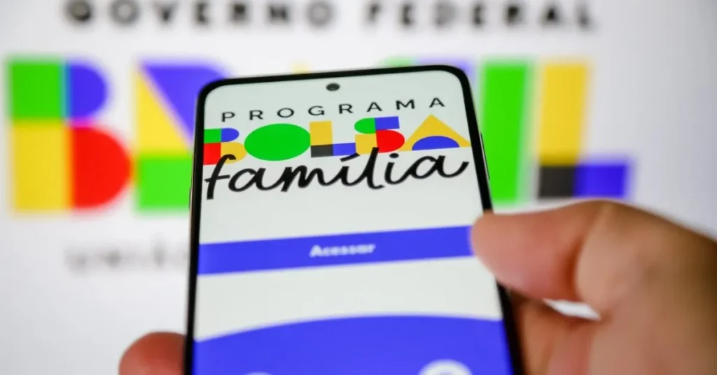 Mãos segurando celular com informações de pagamento do Bolsa Família de agosto de 2026