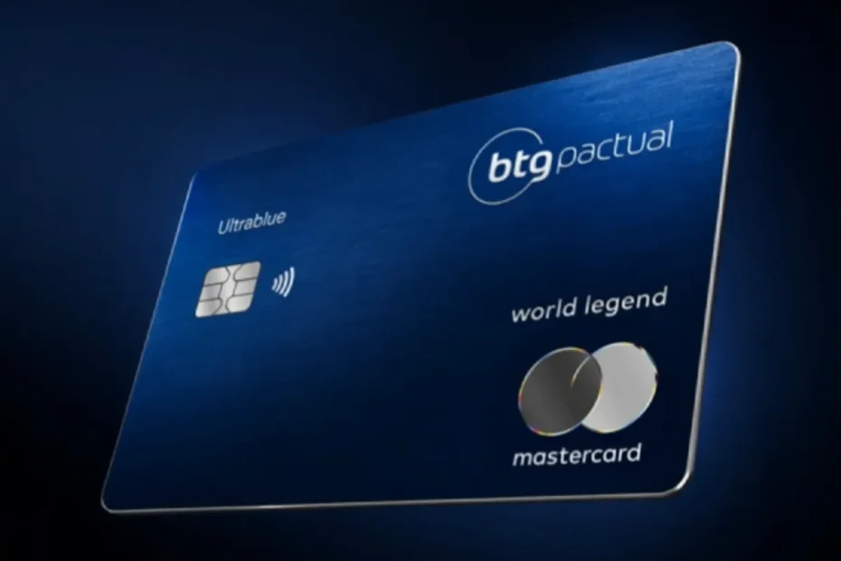Mão elegante segurando o cartão de crédito BTG Pactual Ultrablue World Legend em um lounge VIP de aeroporto, com taça de vinho e ambiente luxuoso ao fundo.