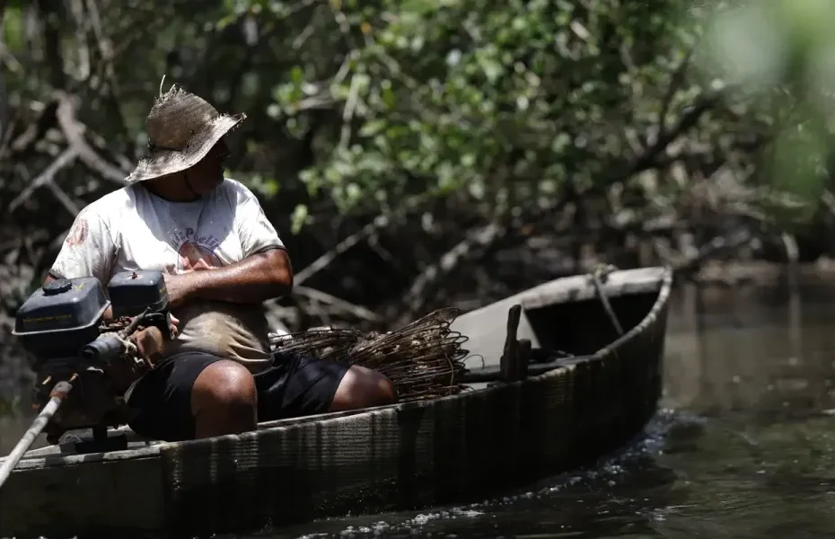 Pescador artesanal consulta pagamento do INSS em celular à beira-mar