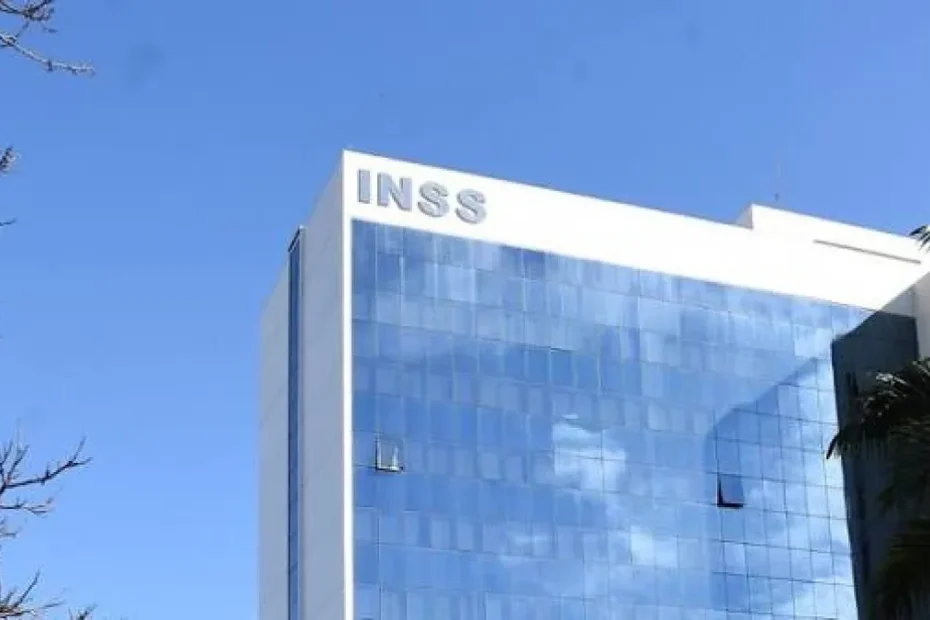 Mãos de servidor do INSS digitando em computador, com formulários de benefícios no fundo