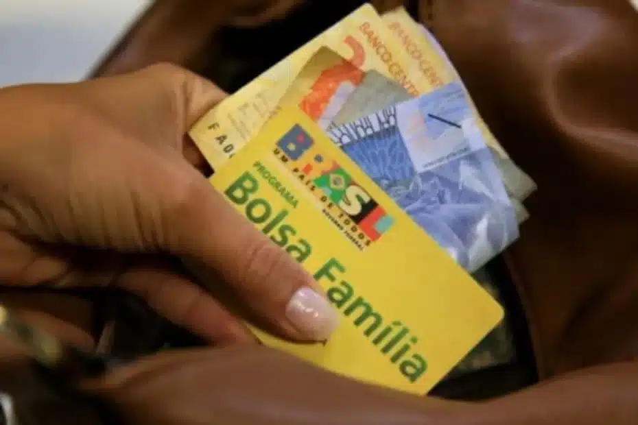 Pessoa preocupada olhando informações do Bolsa Família no celular com documentos espalhados na mesa.