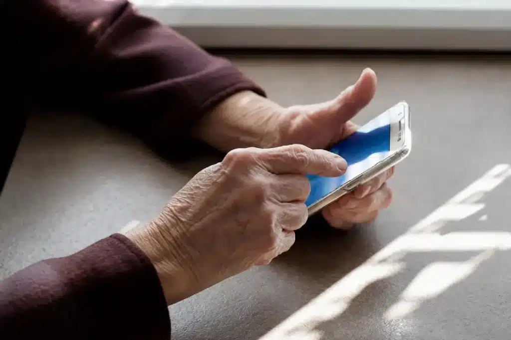 Mãos de um aposentado segurando um celular com expressão preocupada, simbolizando um golpe financeiro digital