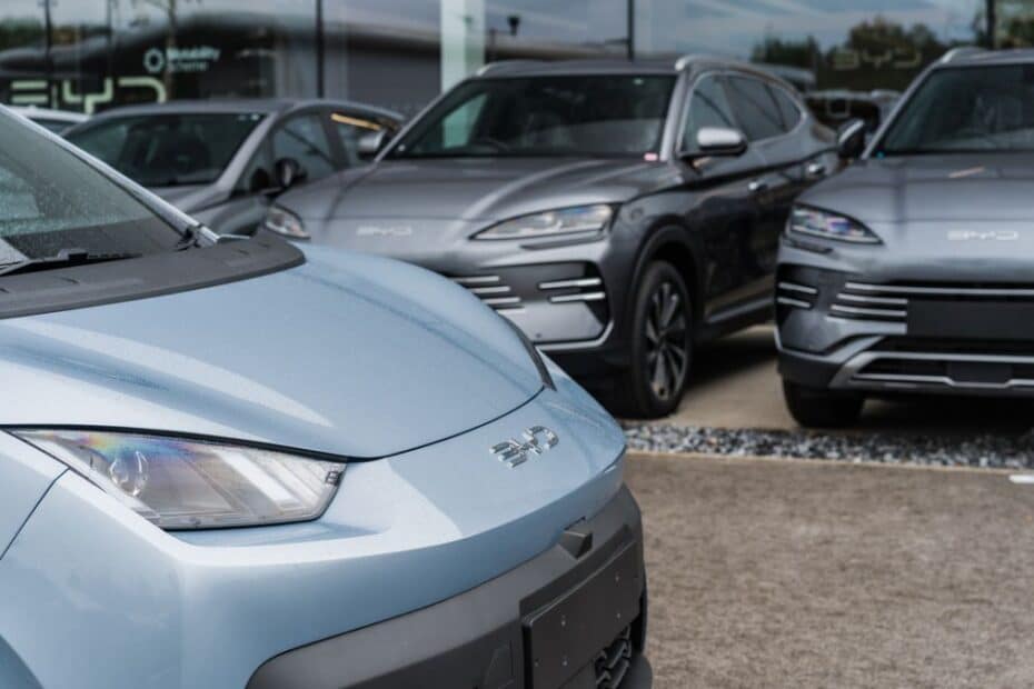 Motorista de aplicativo sorri ao lado de um carro elétrico BYD novo, com logo do Banco do Brasil ao fundo, simbolizando a facilidade de financiamento.