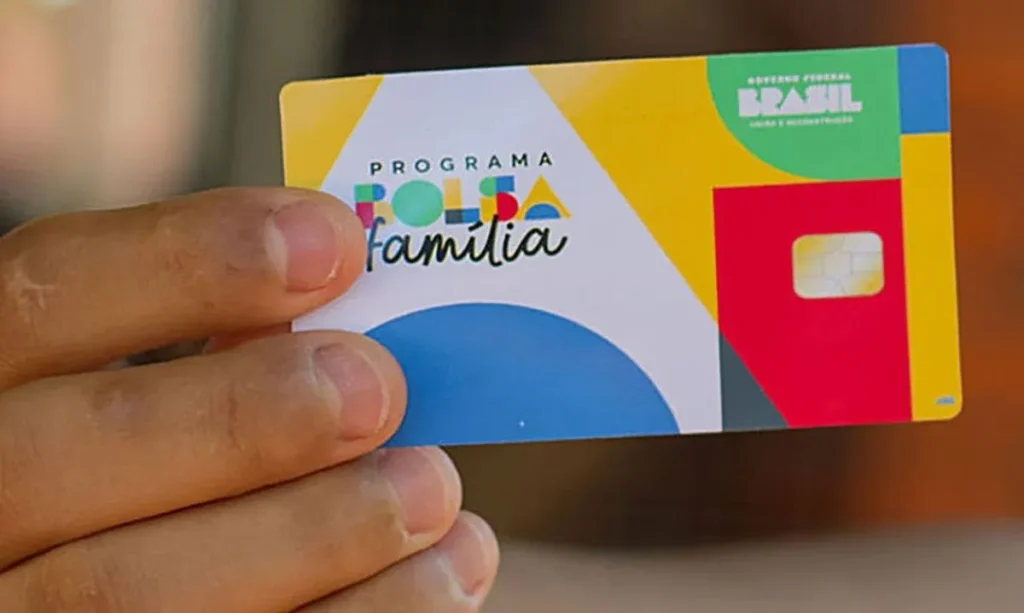 Mulher utilizando o aplicativo CAIXA Tem em um smartphone para acessar o pagamento do Bolsa Família, com crianças ao lado