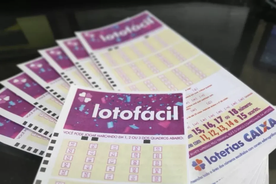 Mãos segurando um bilhete da Lotofácil com números sorteados e prêmio de 5 milhões ao fundo.