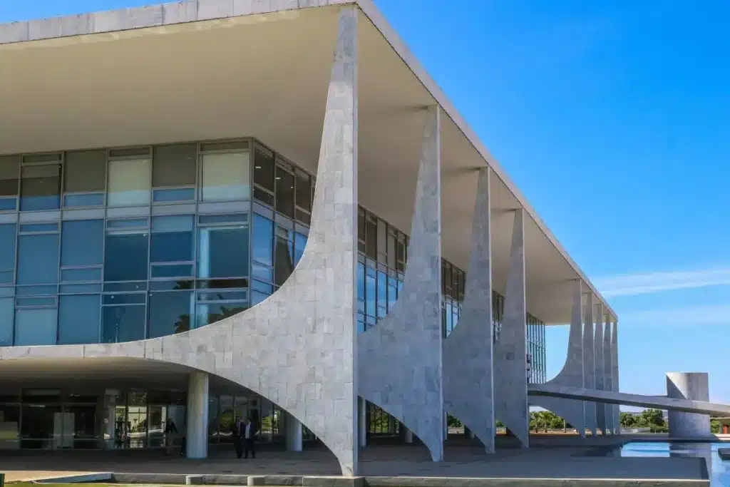 Mãos de adulto e criança segurando água, com infraestrutura de saneamento ao fundo, simbolizando a meta de universalização