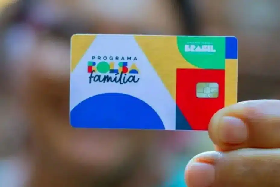 Pessoa utilizando celular para consultar benefício social em frente a uma agência bancária.